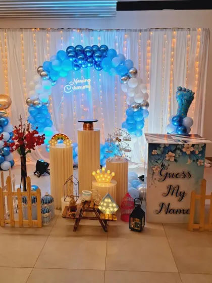 A fun and modern naming ceremony setup with a blue and white balloon arch. The 'Guess My Name' box adds an interactive element for the guests before the name reveal.