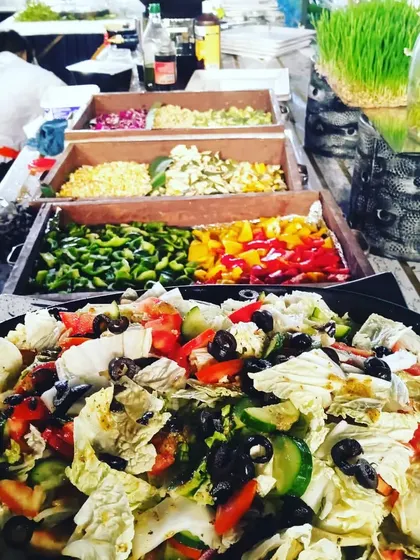 A make-your-own-salad bar with wooden crates holding fresh ingredients like bell peppers, corn, and olives.