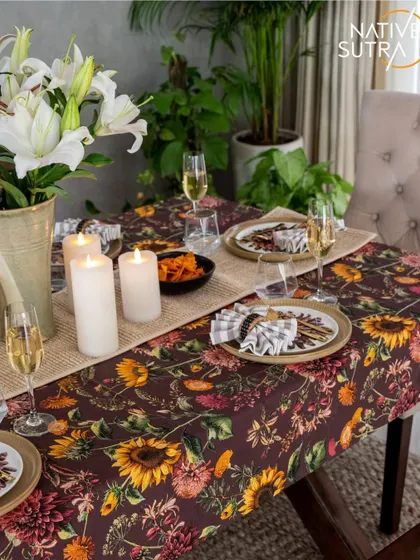 A detail of the beautifully styled tablescape. The rich, floral tablecloth is layered with a natural fiber runner, ceramic plates, and glowing candles, creating an atmosphere of relaxed sophistication.