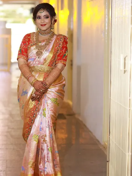 The full look of the soft peach silk saree and the contrasting embroidered red blouse. The combination is traditional yet unique, ensuring the bride stands out on her special day.