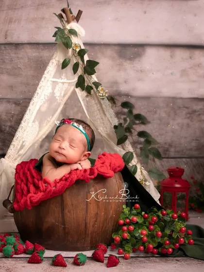 A sweet strawberry-themed session. The baby is nestled in a wooden bucket with a red blanket, surrounded by felt strawberries and a tiny tent.
