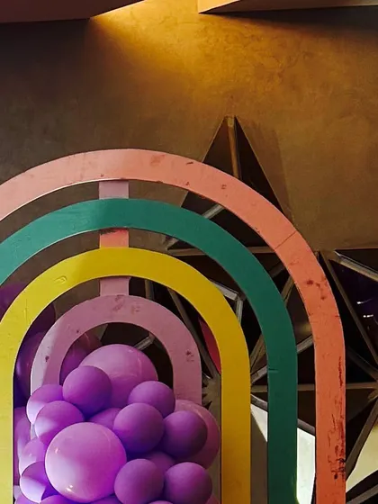 A creative rainbow-shaped wooden prop filled with purple balloons, part of a modern and artistic party design.