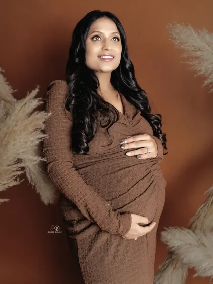 A classic three-quarter portrait of a mom-to-be, beautifully showcasing her baby bump in a comfortable and stylish brown dress. The pampas grass adds a soft, bohemian texture.