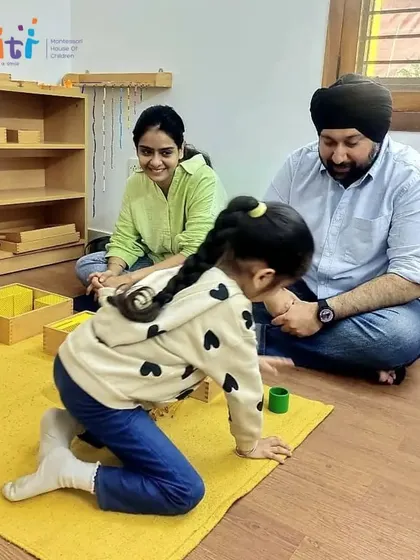 Parents observe their daughter as she works with the golden bead material, learning about quantity and the decimal system. Our classroom is a space for focused, independent discovery.