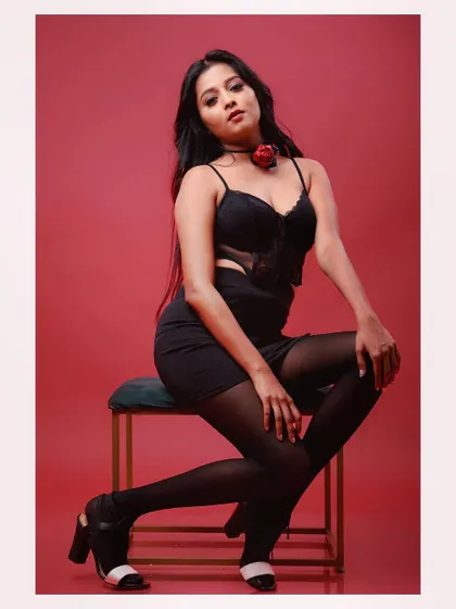 A full-length shot of a model in a glamorous black outfit against a red background. The pose is strong and confident, creating a striking fashion image.