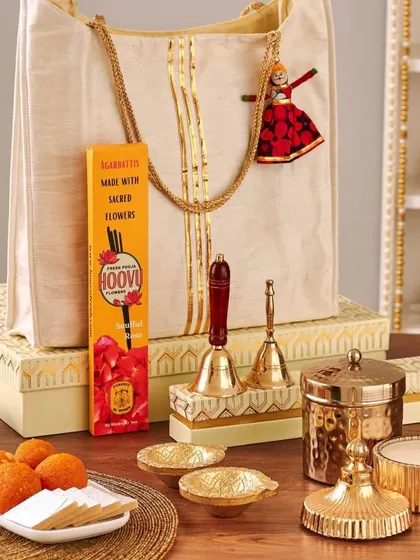 This elegant gift set features a tote bag, a box of Hoovi incense, traditional bells, a lidded brass container, and a plate of laddoos, combining prayer essentials with festive sweets.