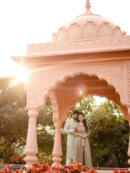 A beautiful pre-wedding portrait under a pink gazebo, with the sun creating a beautiful flare behind the couple.