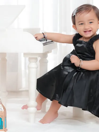 A little musician with a big smile. This shot captures her joy as she sits by the miniature grand piano in a beautiful black dress.