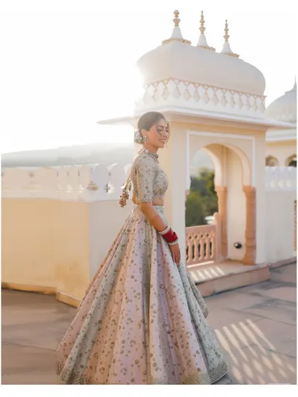 A full-length bridal portrait on the rooftop of The Jaibagh Palace, with the sun setting over the hills.