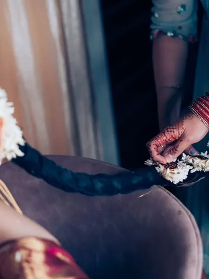 The process of weaving fresh flowers into the bride's traditional braided hairstyle, a beautiful detail of South Indian bridal preparation.