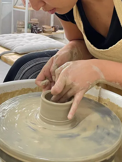 A close-up of a student learning to pull the clay upwards. This technique requires a delicate touch to create even walls for a cup or small vase.