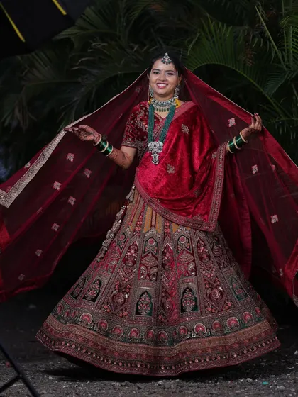 A joyful bride twirling in her stunning wedding lehenga. The rich red velvet and intricate embroidery are captured beautifully in this outdoor shot.