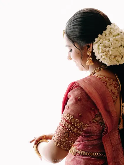 A side profile of the bride, highlighting her beautiful hairstyle with fresh jasmine flowers and the delicate embroidery on her blouse.