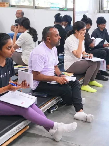 The classroom is a space for active engagement. Students are seen here taking notes and participating in discussions, sitting on Pilates equipment which highlights our integrated fitness environment.