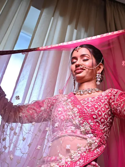 A playful and happy moment. Her radiant makeup and bright pink lehenga come together to create a look of pure bridal joy.