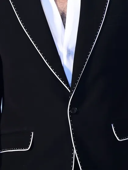 Detail of the lapel and pocket on the custom black suit. The hand-stitched appearance of the white piping adds a touch of artisanal craftsmanship.