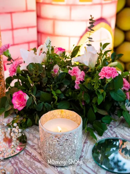 A close-up of a table centerpiece, featuring a candle in a glittering holder surrounded by fresh pink flowers. These small details create a warm and inviting atmosphere for guests.