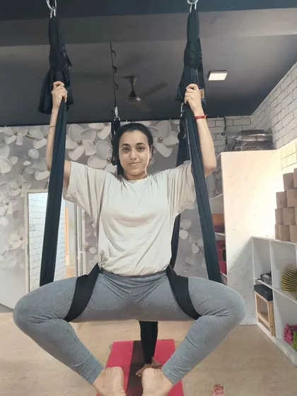 A student demonstrates a supported squat in the aerial hammock, a pose that builds leg strength and stability.