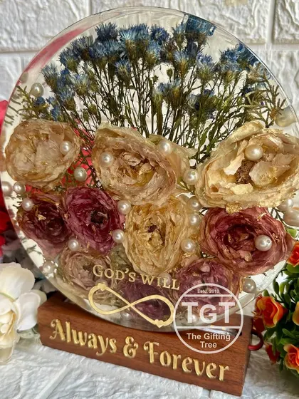 This 8-inch round resin block preserves an engagement bouquet and sits on a custom teakwood stand. The phrase "God's Will" and an infinity symbol are inscribed in gold.