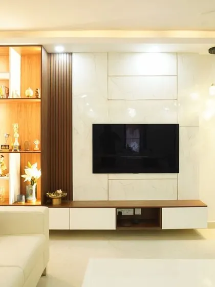 A bright and elegant living room with a white sofa and a custom TV unit. The unit features a tall, backlit display cabinet and a combination of wood and white finishes.