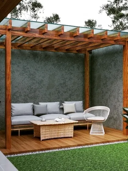 A cozy wooden pergola with a glass-paneled roof, set against a textured concrete wall. The warm tones of the wood deck and wicker furniture create a natural and inviting seating nook.