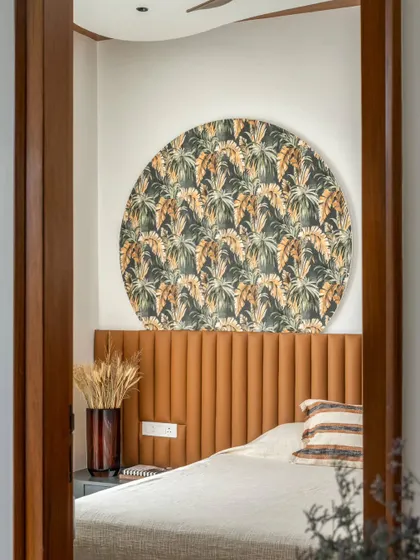 This cozy bedroom embraces the southern sun with earthy hues reminiscent of a lingering sunset. A circular patterned art piece above the fluted leather headboard adds a unique and modern touch to the warm space.