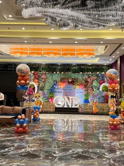 A full view of a jungle safari-themed party in a banquet hall, with themed balloon columns and a large stage backdrop.