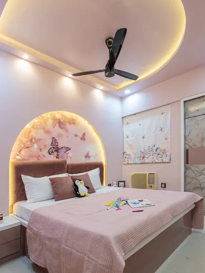 This wider angle shows how the arched headboard, false ceiling with cove lighting, and sliding wardrobe all work together in this pink-themed bedroom.