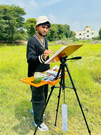 A photo of me painting in a grassy field in rural Bengaluru, fully equipped with my easel and watercolors.