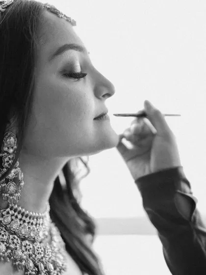 A close-up, black and white shot of the bride getting her makeup done. It's a quiet, focused moment that highlights the artistry and preparation behind the final look.