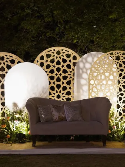 We love playing with patterns and light. This photo booth features a backdrop of backlit jali panels in asymmetric arched shapes, creating a beautiful and intricate setting for pictures.