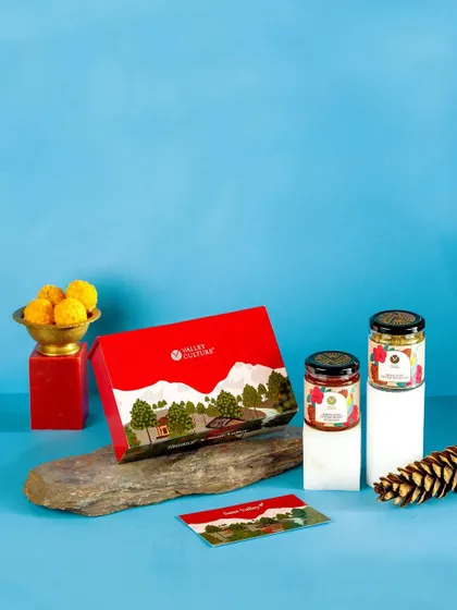 A festive composition for Valley Culture's gift set, featuring traditional Indian sweets (ladoos) and natural elements like a pinecone. The soft blue background provides a calm and pleasant contrast.