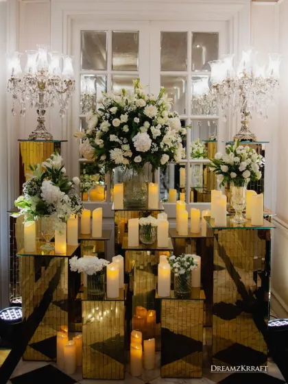 An opulent decor setup featuring crystal candelabras, white floral arrangements, and mirrored gold pedestals. The reflections multiplied the candlelight, creating an incredibly glamorous and radiant effect.