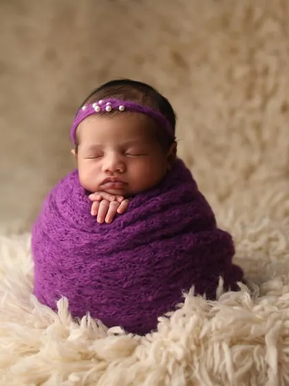 Another variation of the 'potato sack' pose, showing how a simple wrap and headband can create an elegant and beautiful portrait. The focus here is entirely on the baby's serene expression and tiny folded hands.