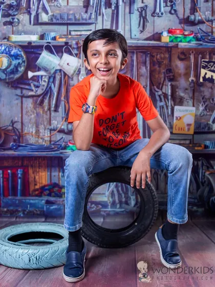 An older boy looking cool and confident in our garage setup. Posing on a stack of tires, he brings a fun and relaxed energy to this creative, tool-filled backdrop.