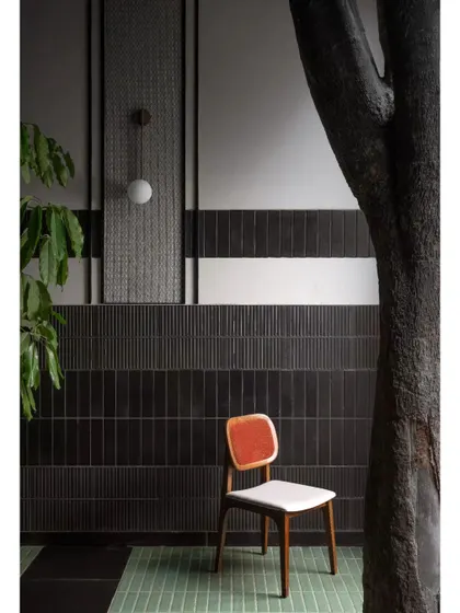A single chair placed against a textured wall next to a tree trunk. This composition highlights the quiet, artistic moments we create within a larger space, focusing on form, texture, and color.