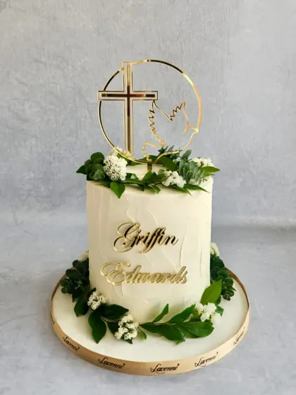 A simple and elegant baptism cake. The textured buttercream is adorned with fresh greenery and a custom gold cross topper.