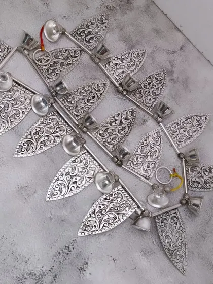 An antique-style German silver door toran, featuring intricately carved leaf-shaped hangings with small bells.