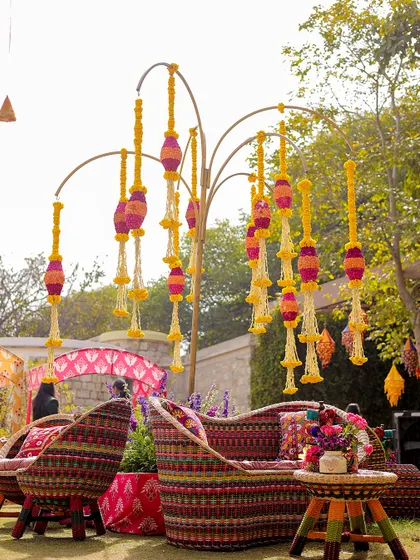 A unique seating arrangement at the carnival, with woven chairs and a tree-like structure adorned with hanging marigold tassels. I focus on creating unique and memorable decor pieces.
