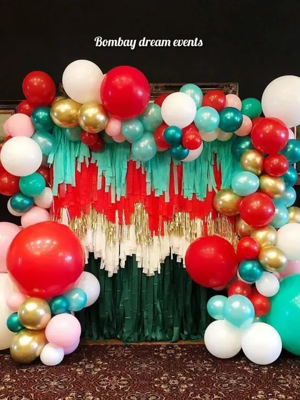 This creative Christmas backdrop uses a fringe curtain in festive colors, framed by a vibrant balloon arch with large red, green, and gold balloons for a fun and modern holiday look.