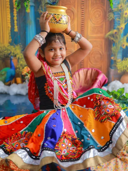 A vibrant portrait of a little Gopi, balancing a pot on her head with a joyful smile. Her colorful dress and the festive setup make this a truly stunning image.
