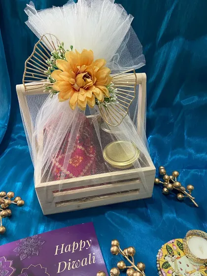 A rustic wooden crate hamper beautifully wrapped in white tulle with a large flower. This Diwali gift combines natural aesthetics with festive goodies inside.