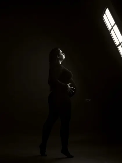 An artistic shot showing the studio setup. The client is silhouetted against the bright studio light, creating a powerful and modern black and white image that feels both raw and beautiful.
