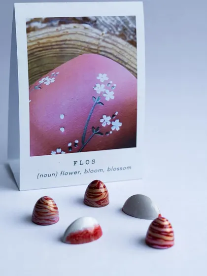 'Flos', meaning flower. These delicate bonbons are inspired by blossoms, combining subtle color gradients and intricate patterns to create a beautiful, edible flower.