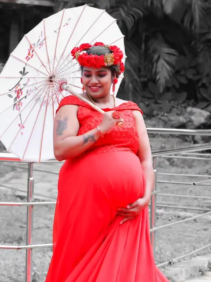 A creative maternity photo with a color splash effect, highlighting the mother-to-be in a red gown holding a traditional umbrella.