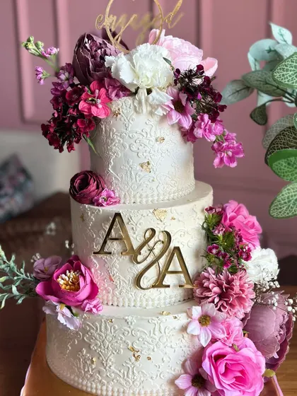 This exquisite three-tiered engagement cake features a pristine white finish with delicate, hand-piped details. A cascade of exotic, vibrant flowers adds a perfect contrast, symbolizing a love that is both pure and full of life.