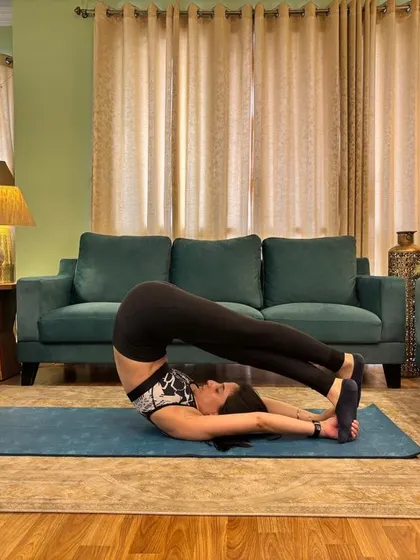 Plough pose on the rug at home, feet over my head and arms long on the mat.