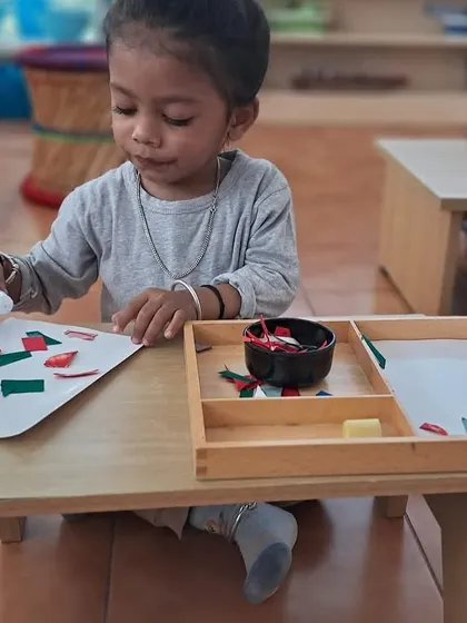A child engages in a paper-cutting activity, which requires focus and fine motor control. This is a practical skill that also builds concentration and hand strength.