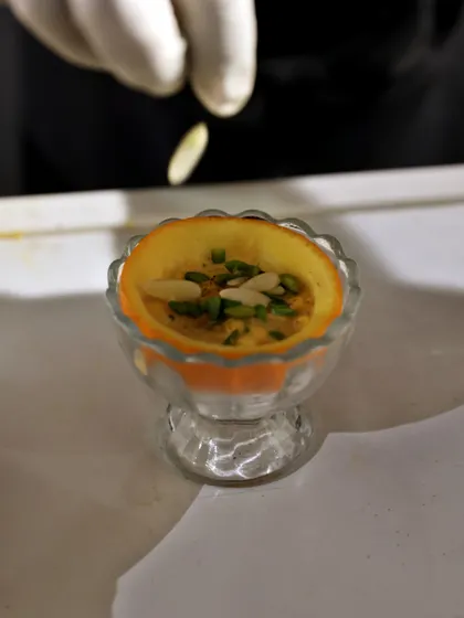 A chef adds the final touch of slivered almonds to a saffron-infused dessert served in an orange cup. This is an example of our creative and culturally-inspired sweet offerings.