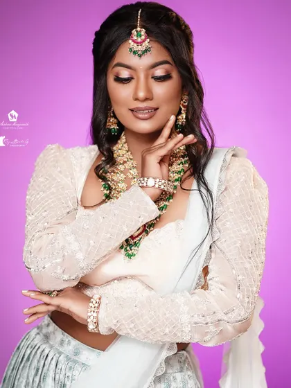 A stunning look on a dusky skin tone, featuring a white lehenga and beautiful green and red jewelry.